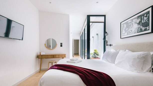 Een moderne hotelkamer met een groot bed, een nachtkastje, een spiegel en uitzicht op de gang.