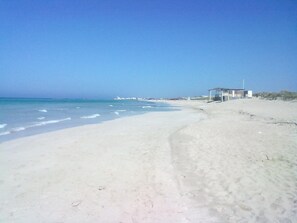 A beach with a clear sky, sandy shore, and a small building in the distance. - SEPTEMBER IN SALENTO: VILLA 70 METERS FROM THE SEA.  (Torre San Giovanni)
