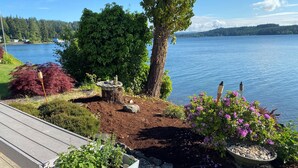 Una terraza con vista a un lago, rodeada por un jardín con diversas plantas y un bebedero para pájaros.