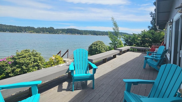 Una terraza de madera con sillas Adirondack turquesa y vistas a un lago.