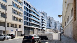 Eine moderne Stadtstraße mit mehrstöckigen Wohngebäuden, einem Parkplatz und blauem Himmel.