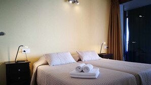 Een hotelkamer met twee bedden, een nachtkastje met een lamp en een raam met gordijnen.