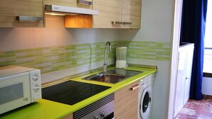 Een kleine keuken met een magnetron, kookplaat, spoelbak en wasmachine.