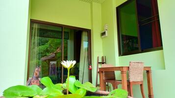 A room with a large window, a potted plant with a white flower, and a wooden chair.
