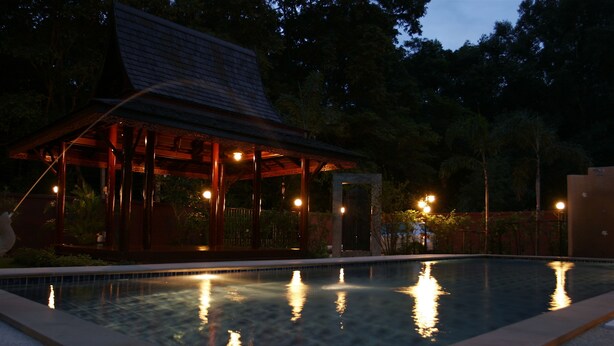 Ein Schwimmbecken mit einer Holzterrasse und einem überdachten Pavillon.