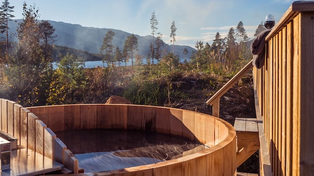 Een houten jacuzzi met uitzicht op een meer en bergen.