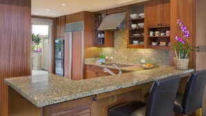 Eine moderne Küche mit Granitarbeitsplatten, Holzschränken und einem eingebauten Backofen. Zwei Barhocker und eine Spüle mit Armatur sind vorhanden.