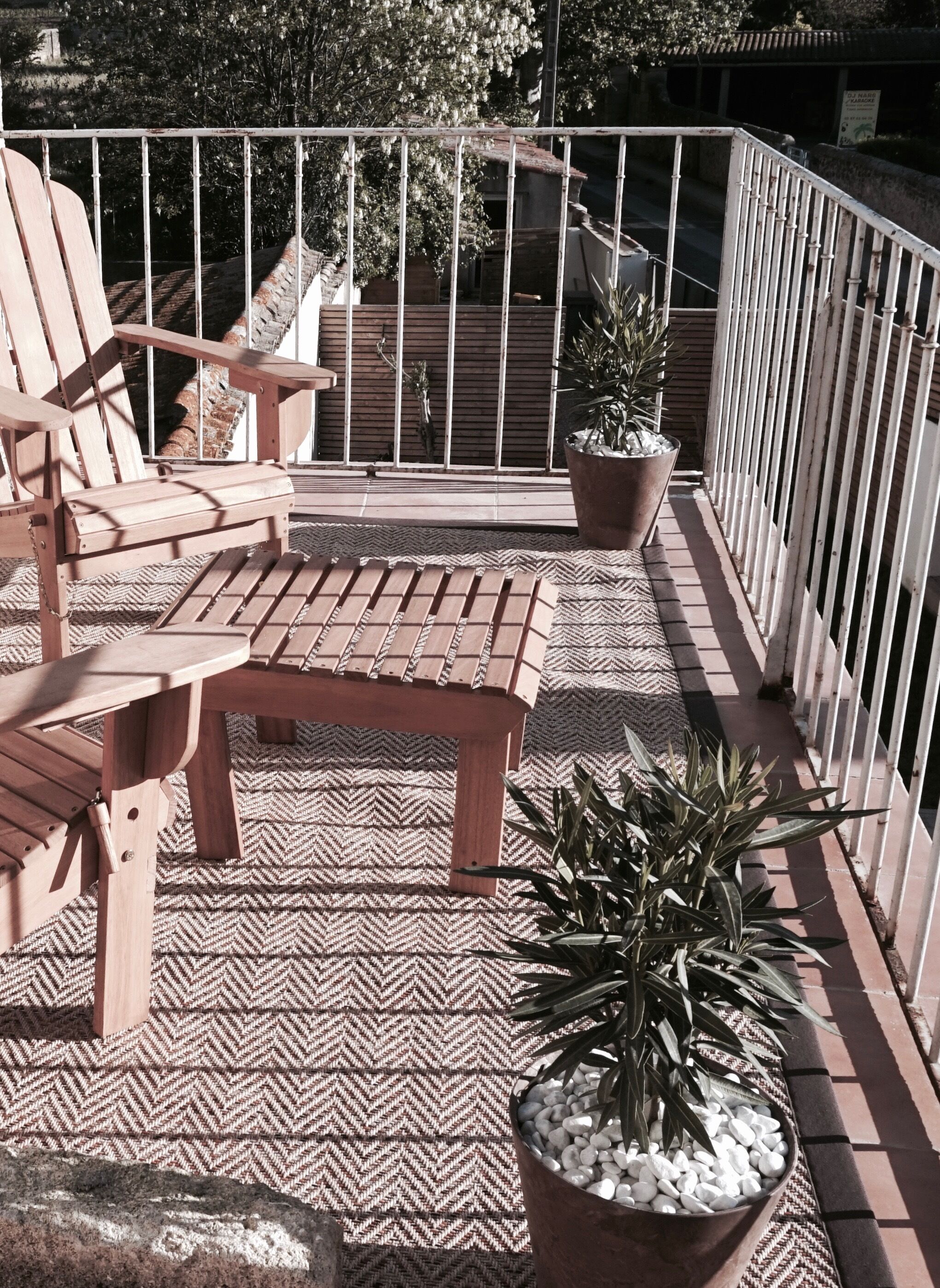 Un balcon avec une chaise en bois, une petite table et des plantes en pot.