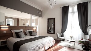 A modern bedroom with a large bed, a sitting area with a chair, a small table, and a potted plant. - Maison d'hôtes La Domitia (Montbazin)