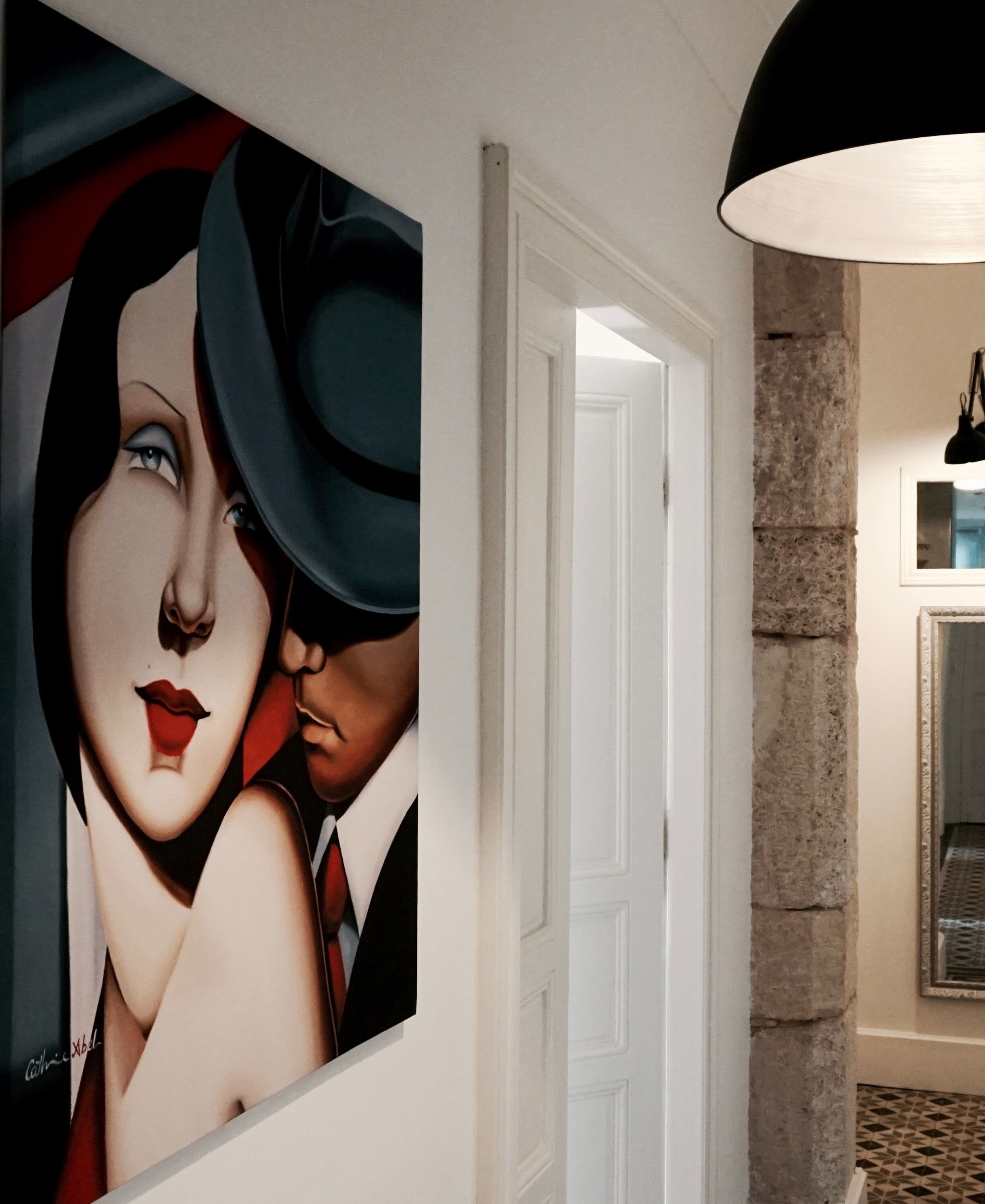 Un couloir avec un grand tableau, un pilier en pierre et une porte.