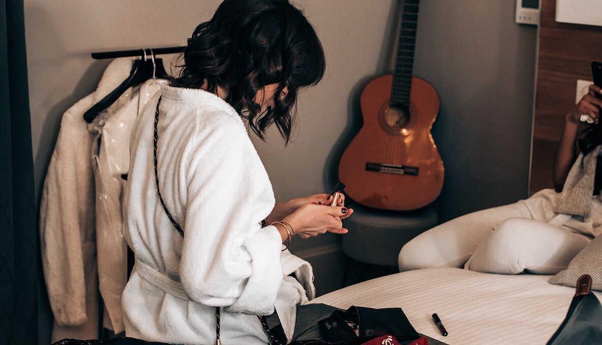 A person sitting on a bed in a room with a guitar and a coat rack.
