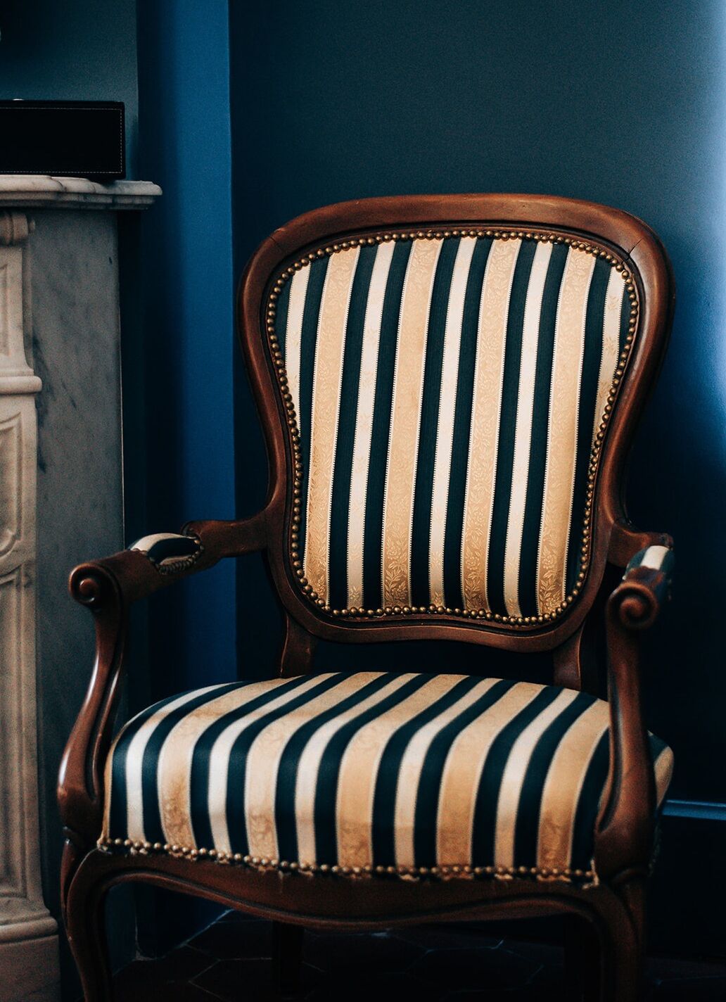 A wooden chair with a striped upholstered seat and backrest, positioned against a blue wall.