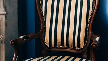 A wooden chair with a striped upholstered seat and backrest, positioned against a blue wall.