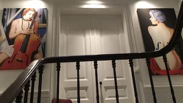 Un escalier avec une rampe, une chaise rouge et deux tableaux accrochés aux murs.