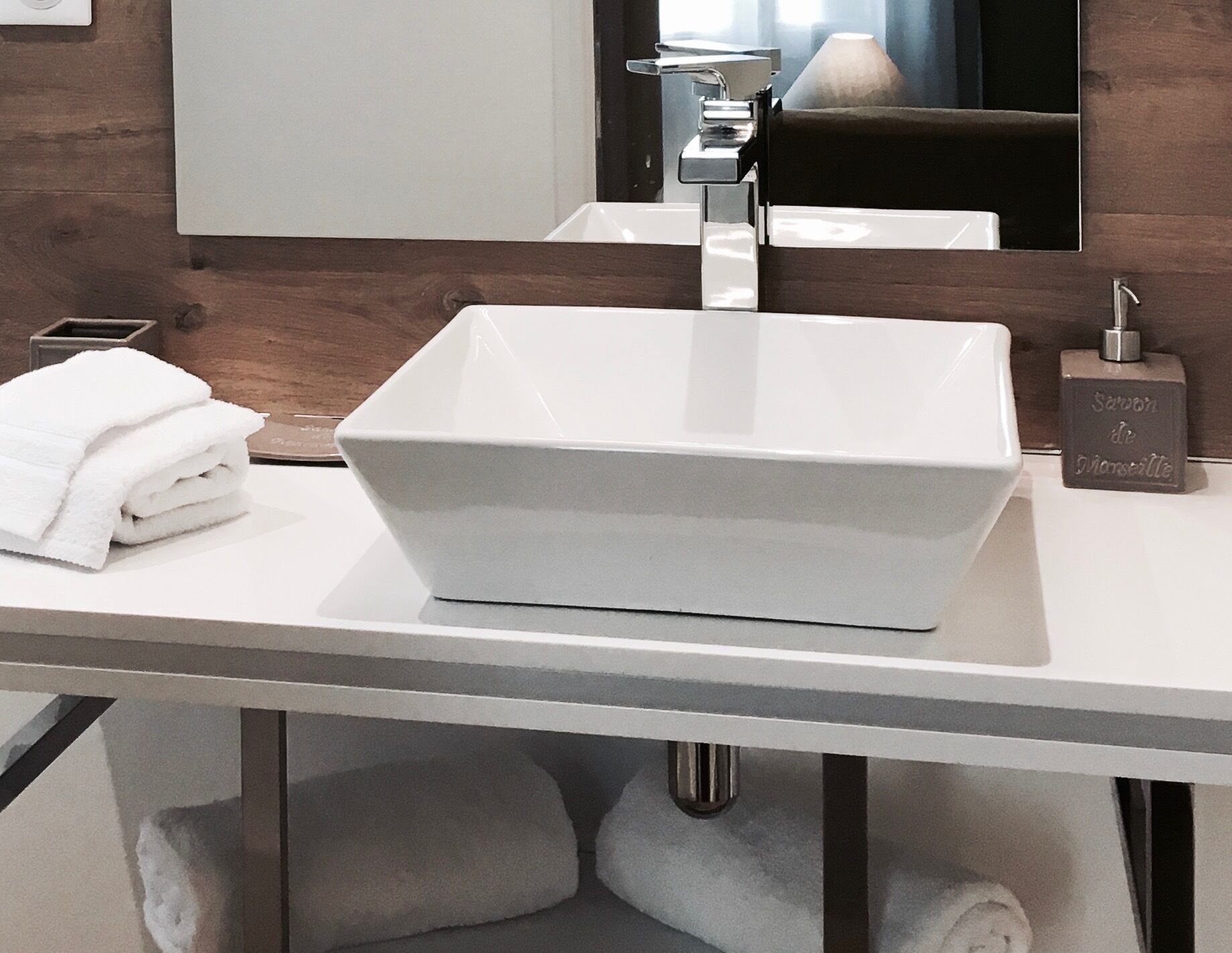A modern bathroom with a white rectangular sink, a mirror above it, and a towel dispenser on the right.