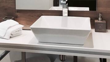 A modern bathroom with a white rectangular sink, a mirror above it, and a towel dispenser on the right.