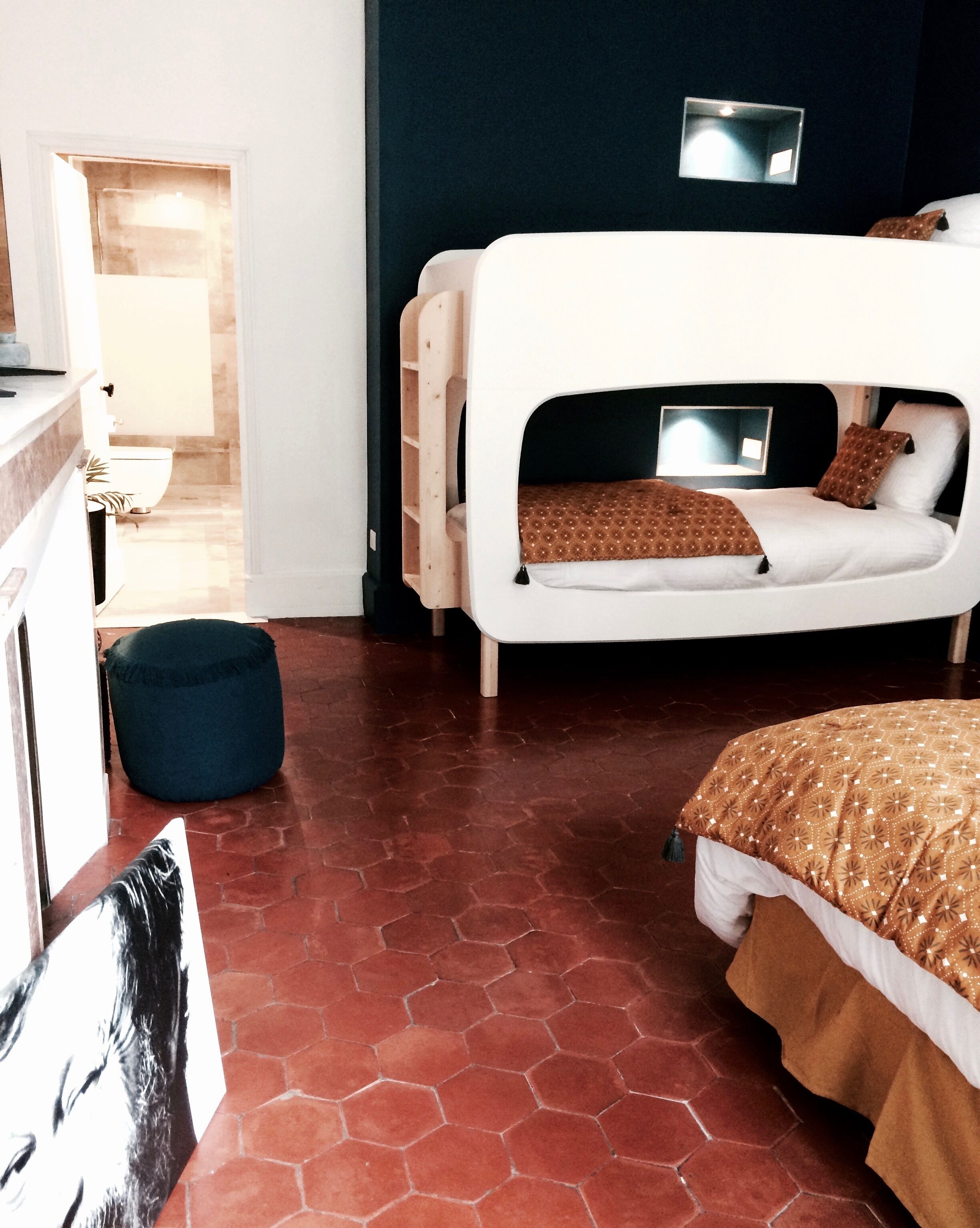 Une chambre avec un lit superposé, un bureau et une chaise. On y trouve un petit pouf bleu et une armoire blanche.