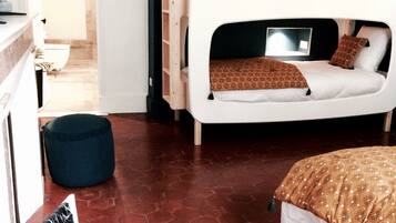 Une chambre avec un lit superposé, un bureau et une chaise. On y trouve un petit pouf bleu et une armoire blanche.