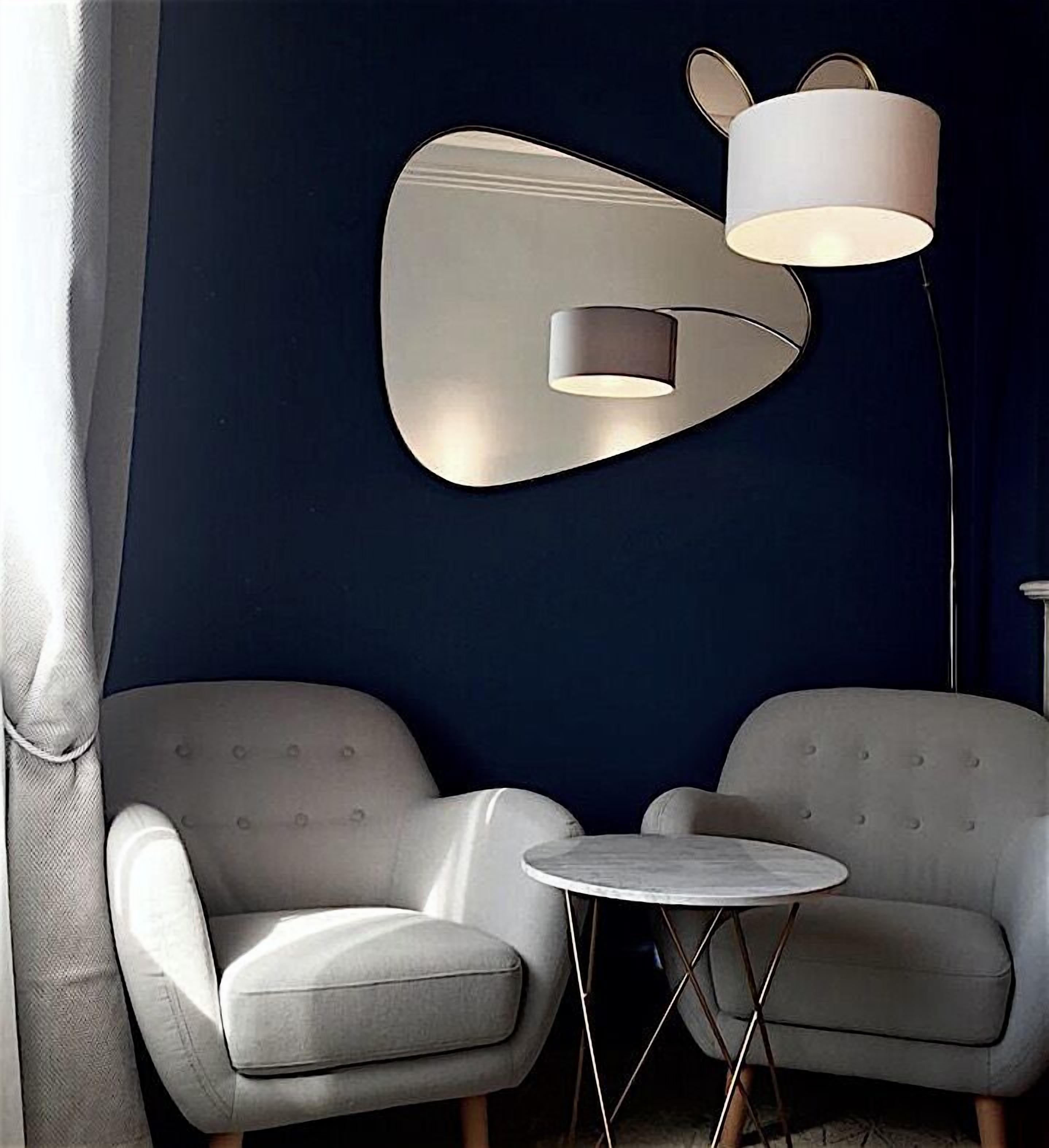 A modern room with two grey armchairs, a small round table, and a wall-mounted lamp.