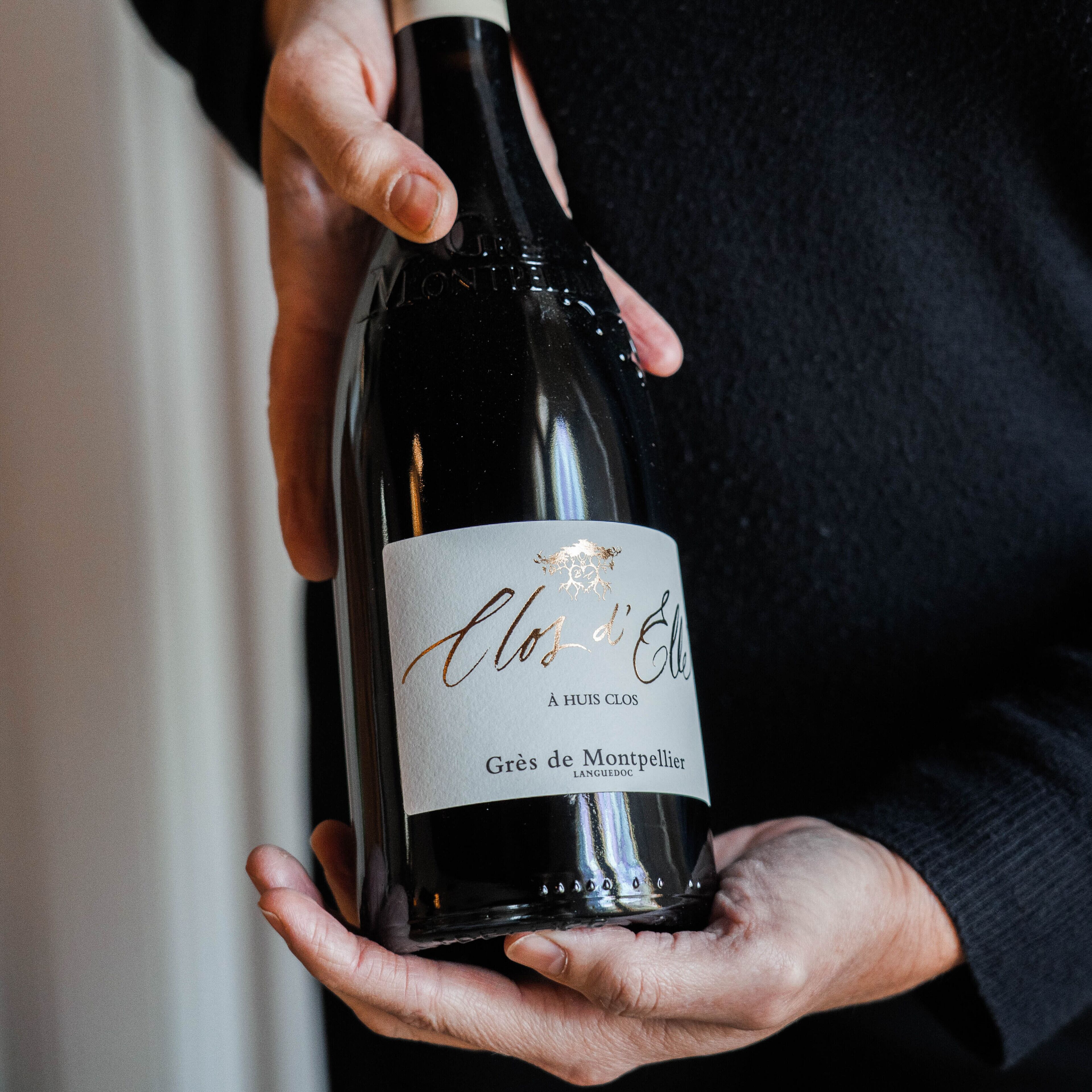 A person holding a bottle of wine with a label that reads "Clos d'Elles."