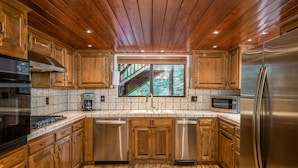 A kitchen with wooden cabinets, stainless steel appliances, and a window overlooking a forest.