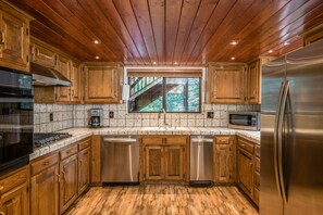 A kitchen with wooden cabinets, stainless steel appliances, and a window overlooking a forest. - Johnson's Firefall Lodge - 2 miles from Yosemite National Park! (Fish Camp)