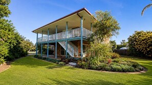 A two-story house with a balcony, surrounded by a well-maintained lawn and various plants.