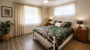 Un dormitorio con una cama, dos mesitas de noche, un velador, un ventilador de techo y una ventana con cortinas.