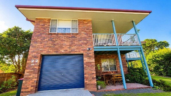 A two-story house with a blue garage door, a balcony with a railing, and a number '22' on the door.