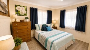 A bedroom with a bed, dresser, nightstands, lamps, curtains, and a wall-mounted picture.