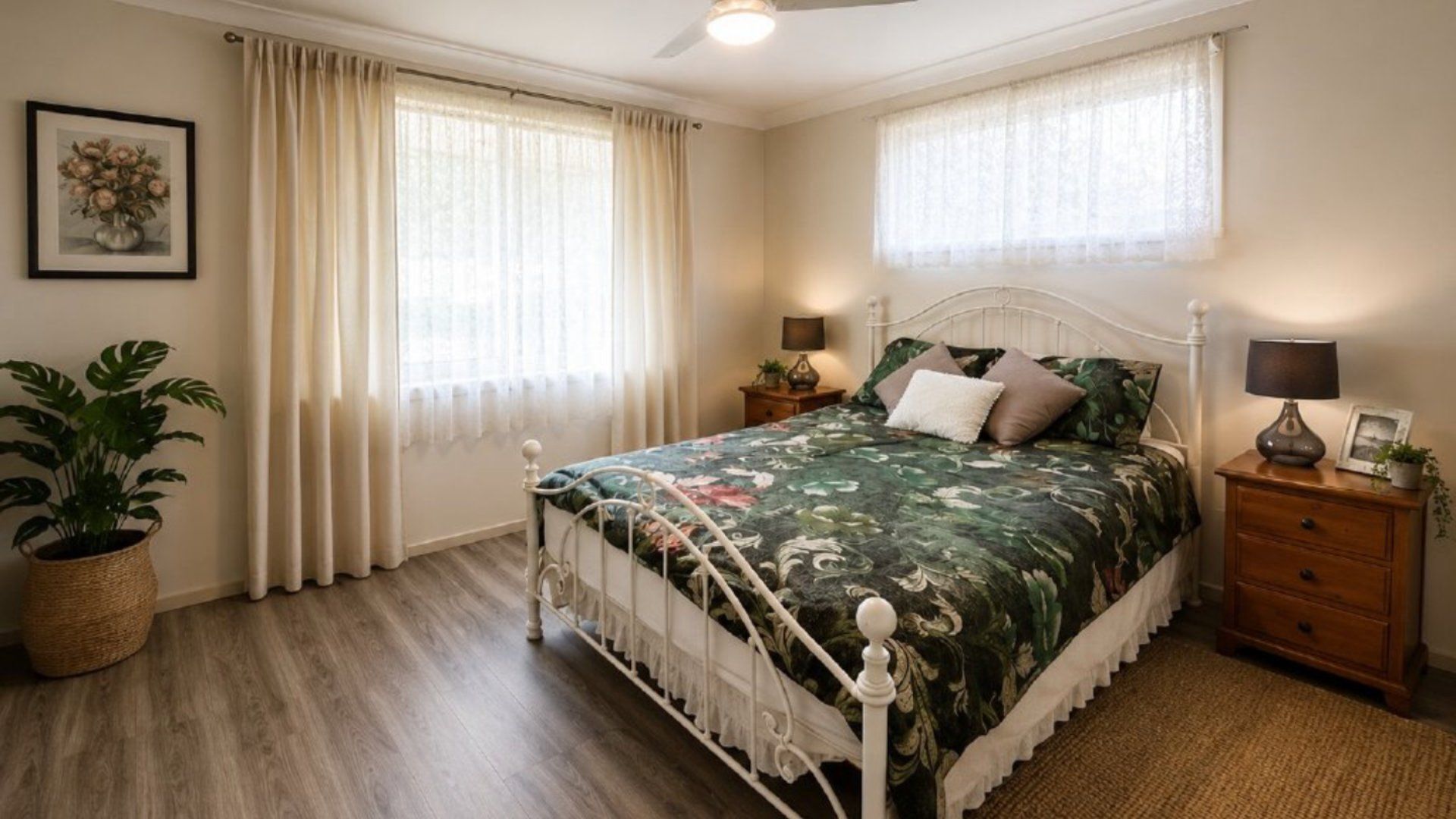 A bedroom with a bed, two bedside tables, a nightstand, a potted plant, and a window with curtains.