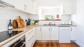 A modern kitchen with white cabinetry, a built-in oven, a dishwasher, and a window providing natural light.