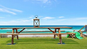 Un espace de pique-nique aménagé au bord de la plage, avec des bancs en bois et une lanterne, offrant une vue sur l’océan.