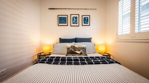 A bed with striped bedding, two bedside lamps, and a wall with three framed artworks.