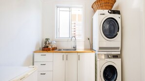 A compact laundry room with a front-loading washing machine, a sink, and a window.