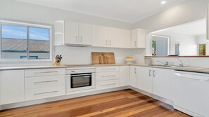 A modern kitchen with white cabinetry, a wooden floor, and a window with a view of a building.