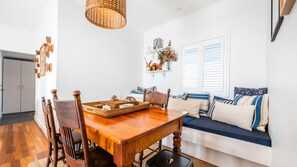 A dining area with a wooden table and chairs, a woven light fixture, and a blue sofa with patterned cushions.
