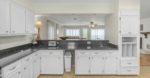 Enjoy cooking in this well-equipped kitchen with a central island, white cabinetry, and a large window offering a view of the living area.