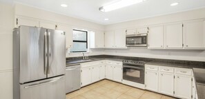 Enjoy cooking in this well-equipped kitchen with a refrigerator, microwave, and oven, set against a backdrop of white cabinetry and a granite countertop.
