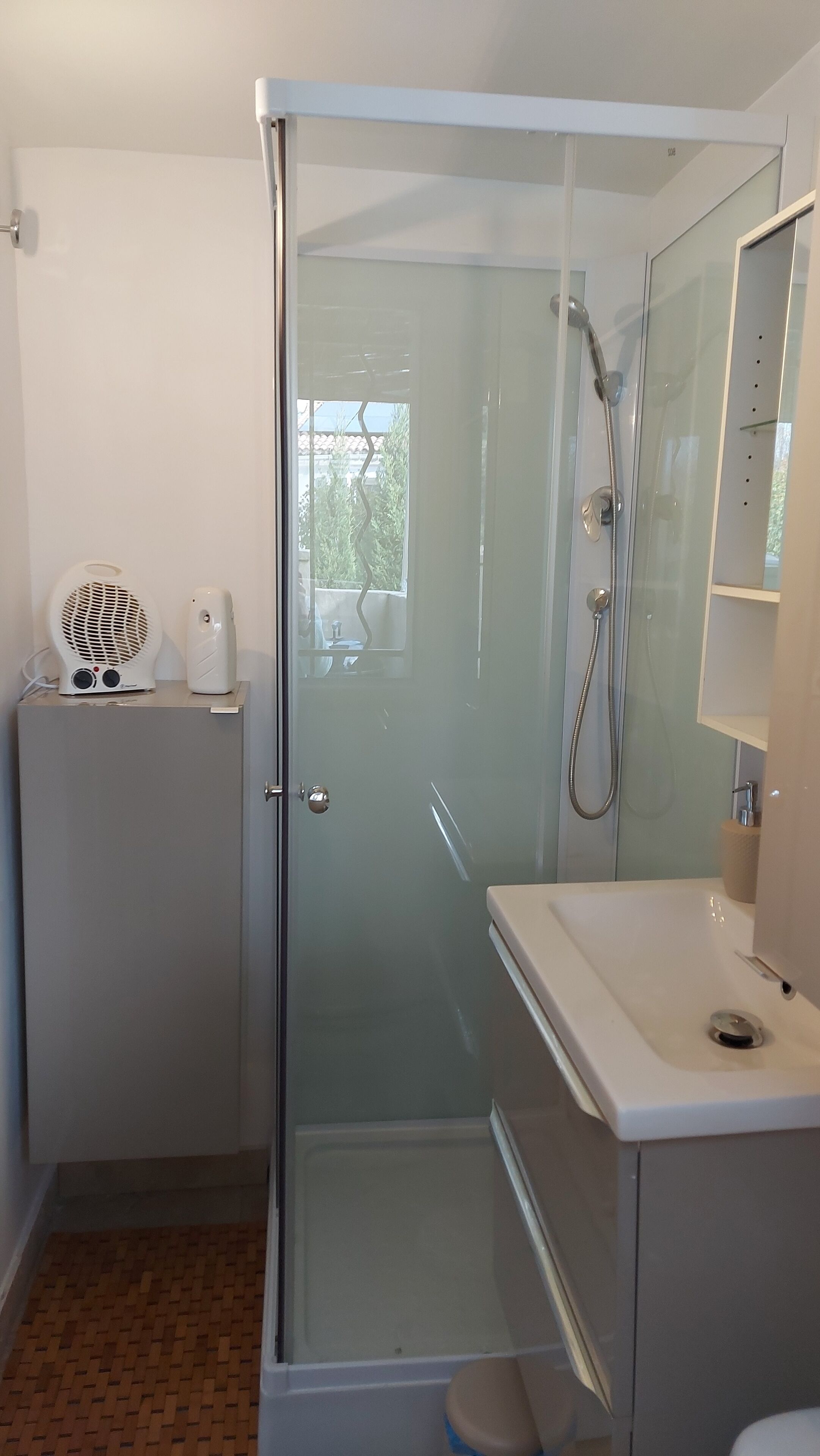 Une salle de bain moderne avec une douche à parois de verre, un lavabo blanc et un petit ventilateur fixé sur un meuble.