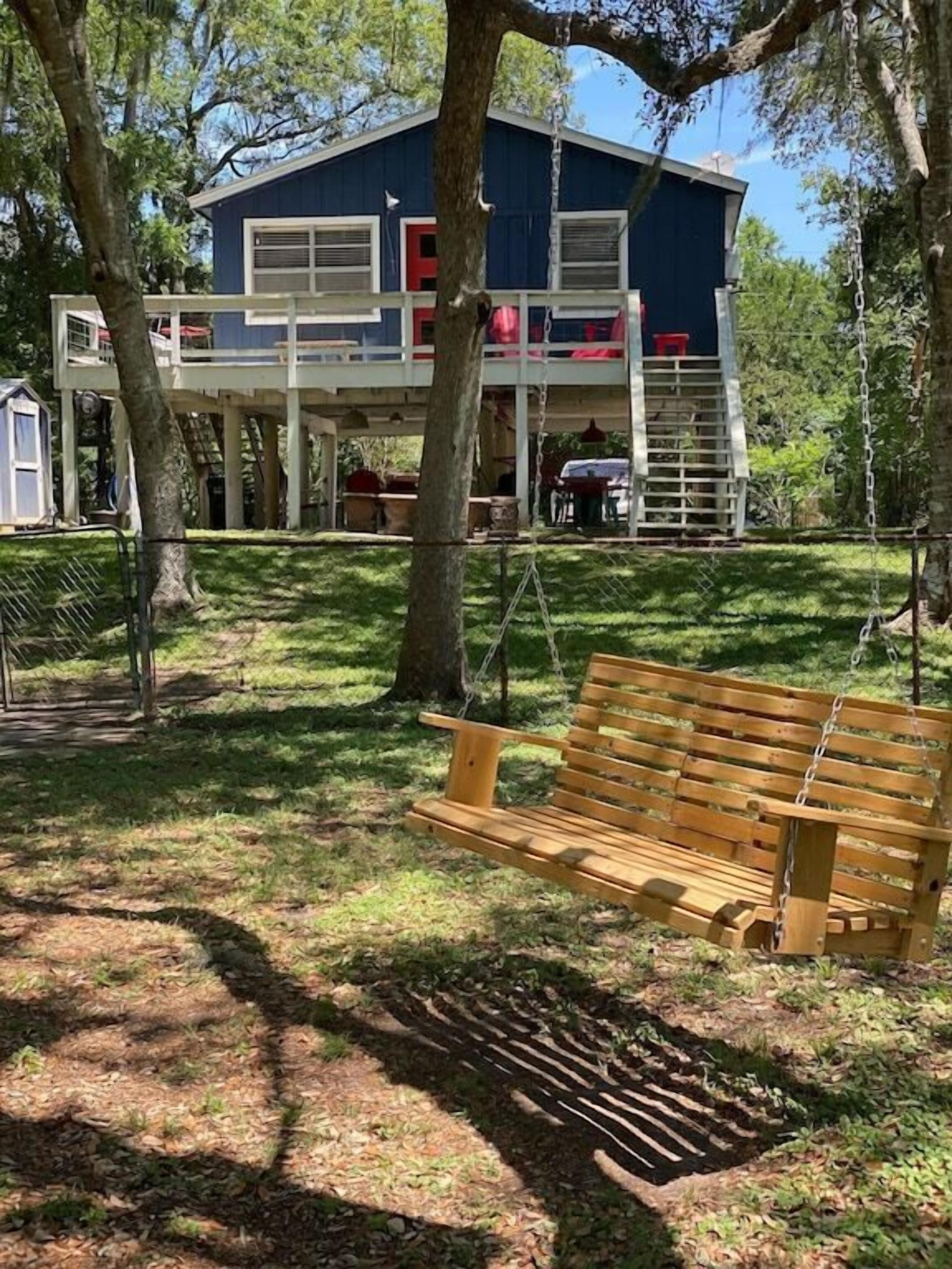 A two-story house with a porch, a swing set, and a wooden bench.