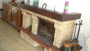 Una chimenea de piedra con repisa de madera, un mueble de madera a la izquierda y una cesta de mimbre a la derecha.