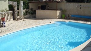 Una piscina rectangular con agua azul cristalina, rodeada de baldosas de piedra y un muro de piedra.