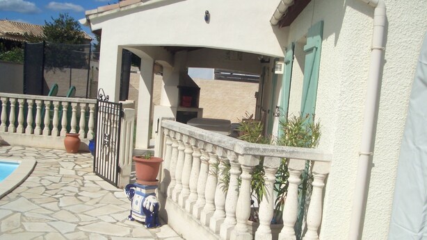 Un patio con piscina, suelo de piedra, una reja y plantas en macetas.