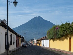 A cobblestone street lined with colorful buildings, a mountain in the background, and a street lamp.