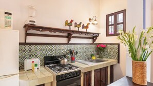 Cozinha com fogão, forno e pia. Há um liquidificador e uma torradeira na bancada. Itens decorativos como um vaso com flores e uma prateleira com enfeites de galo colorido também são visíveis.