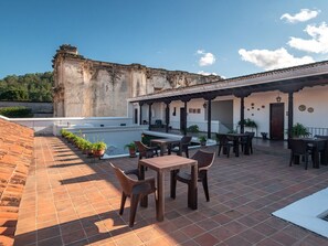 A courtyard with outdoor seating, a tiled floor, and a building with a weathered facade.