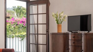 Quarto com cama, um armário de madeira, televisão e janela com vista para flores cor-de-rosa.