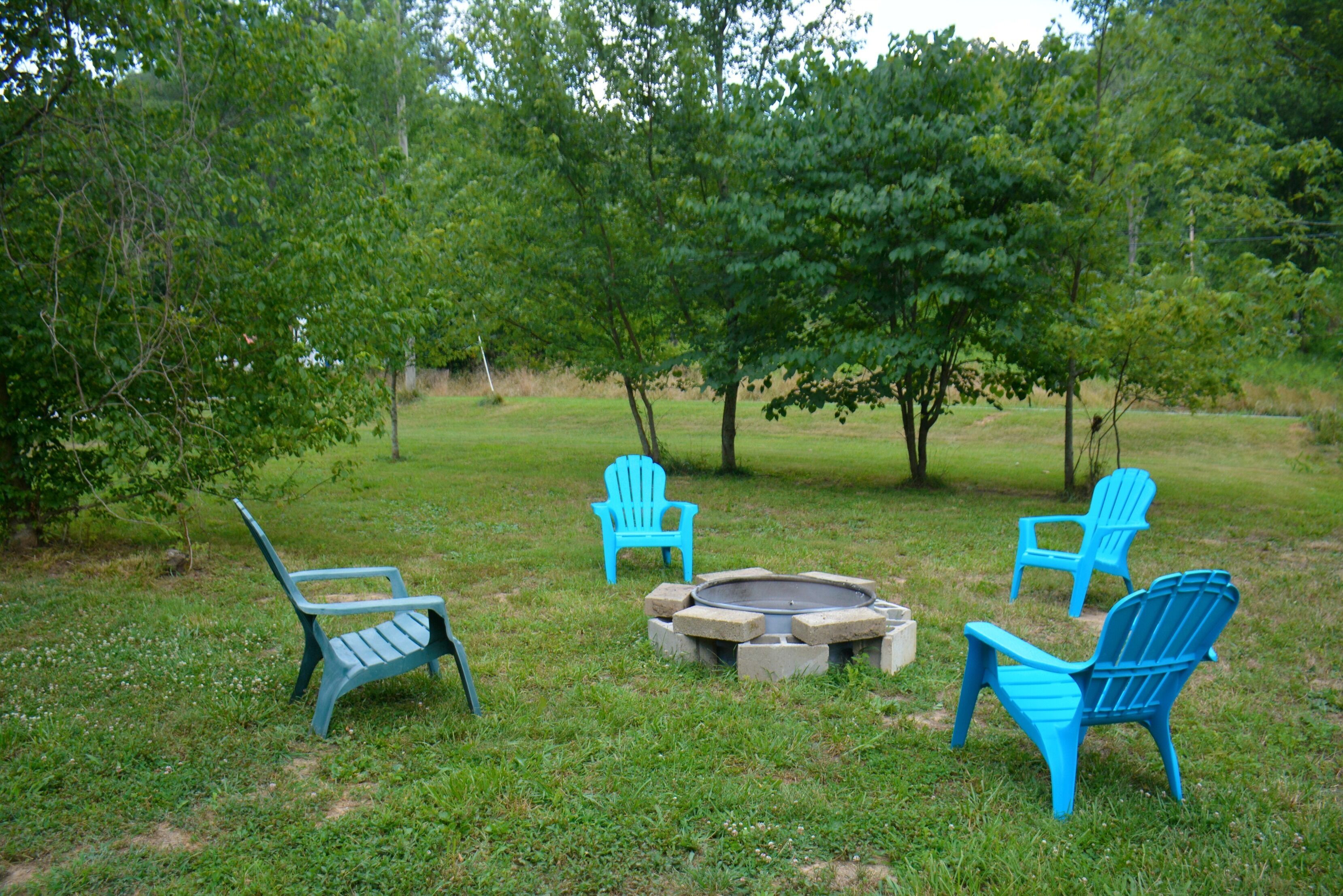 An outdoor seating area with four blue Adirondack chairs and a fire pit.