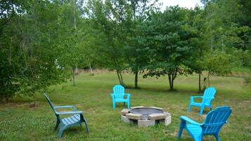 An outdoor seating area with four blue Adirondack chairs and a fire pit.